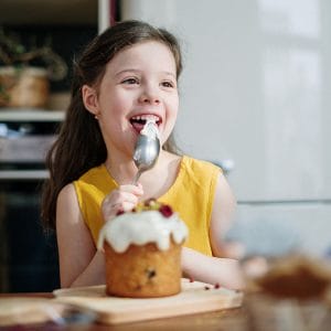 Little girl eating sugary frosting which can lead to cavities.