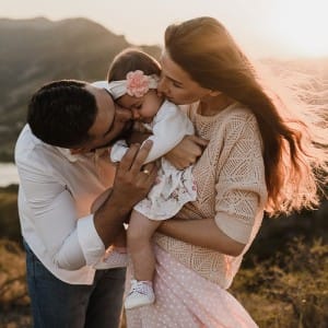 A man and woman kissing a baby on her cheeks even though they have oral bacteria in their mouths.