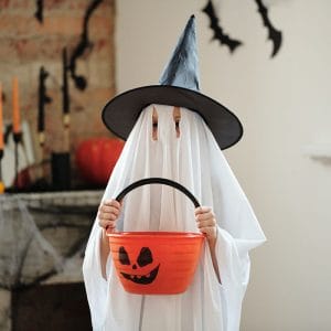A child in a costume holding a plastic pumpkin tub filled with sugary candy. 