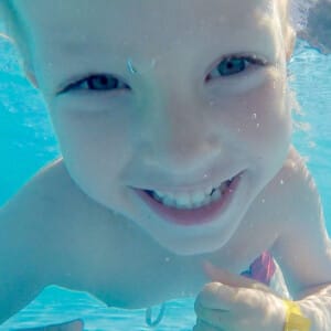 young male child swimming and smiling under water showing his teeth
